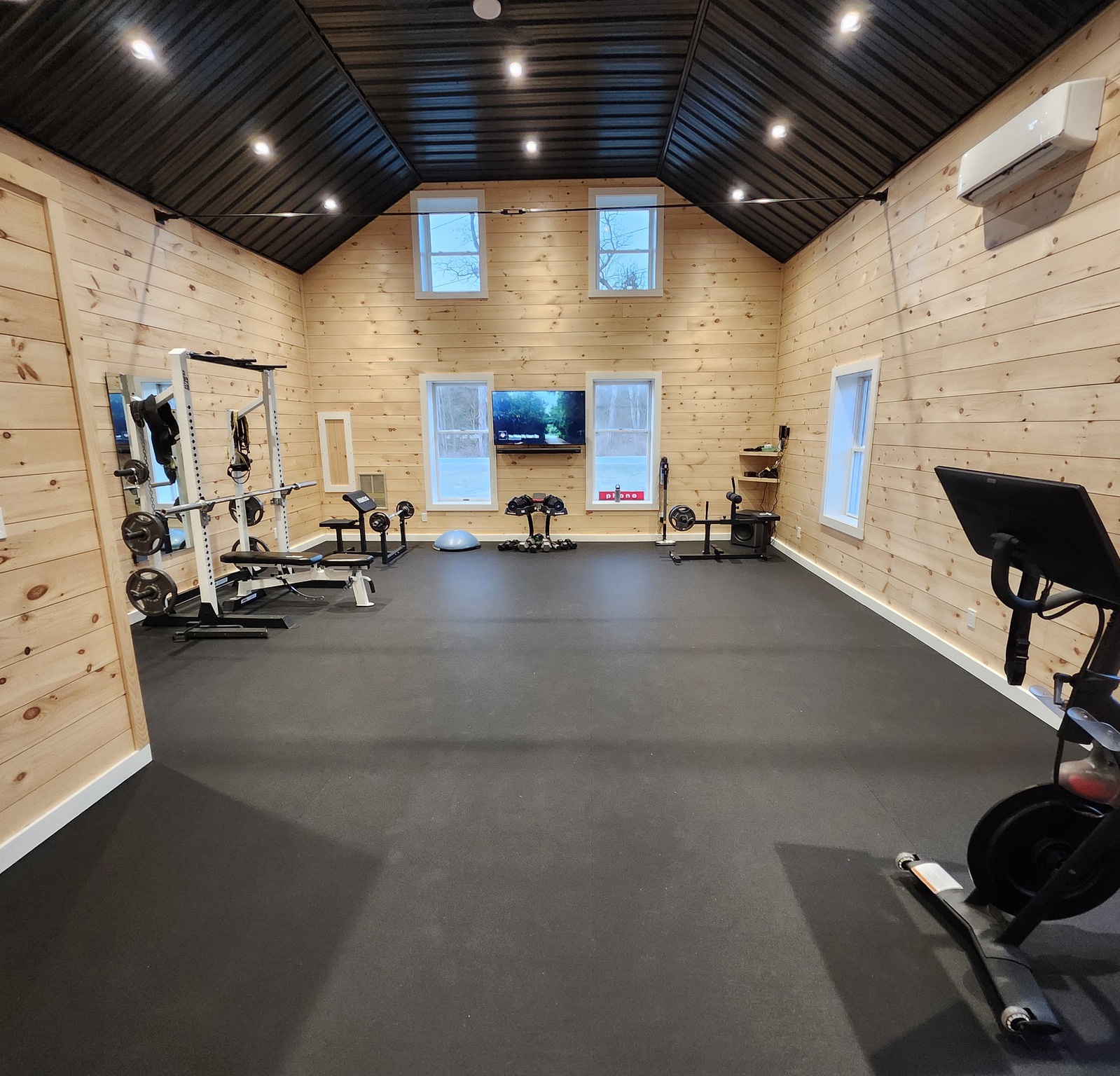 Home gym with timber-clad walls, a high dark ceiling and rubber flooring