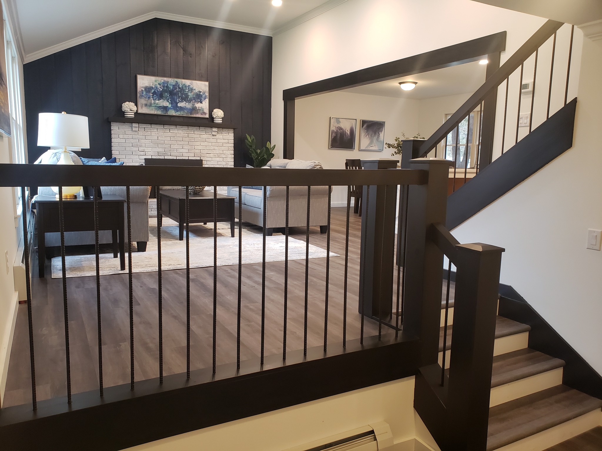 After the remodel: living room with dark trim and railing, a white brick fireplace and a wide opening to the adjoining room