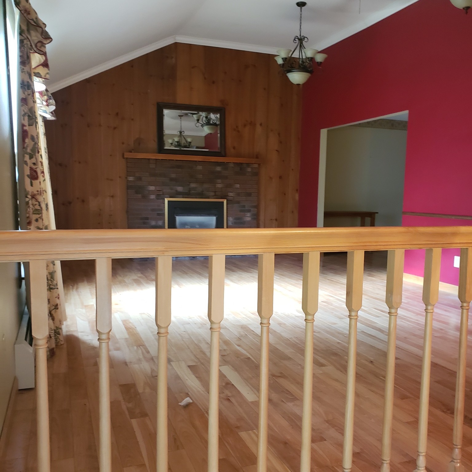 Before the remodel: the same living room with a wooden railing, wood-paneled fireplace wall and red wall with a narrow doorway